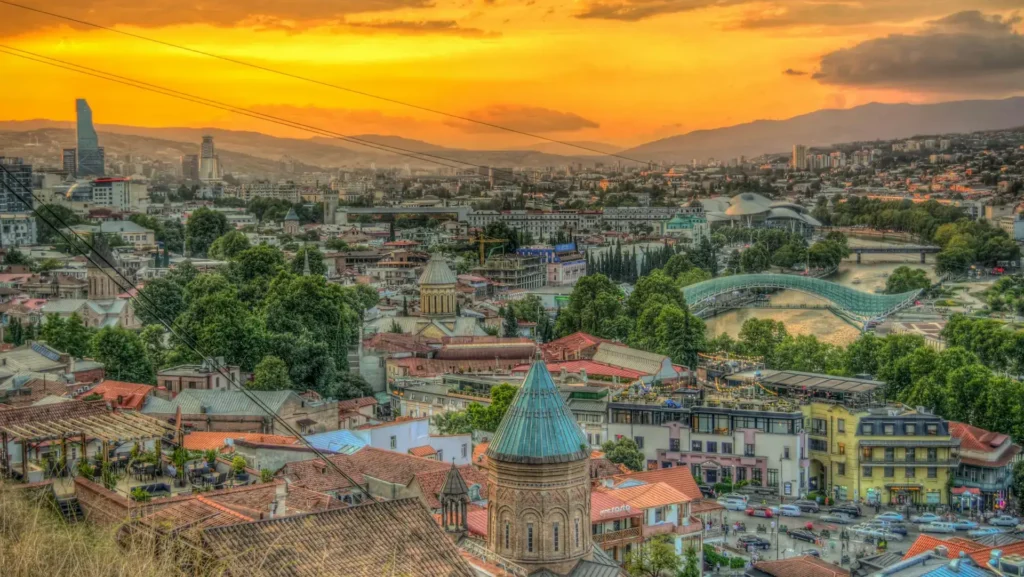 Panoramic view of Tbilisi at sunset: Historic quarters, Narikala Fortress, and the Kura River.